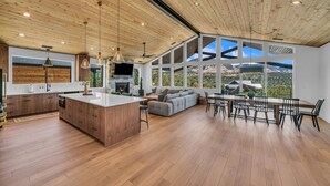A spacious living area with a large window, a wooden ceiling, and a modern kitchen. - High Desert Home | Modern Luxury Near Zion NP (Orderville)