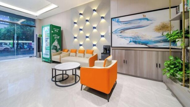 A modern reception area with a sofa, chairs, a coffee machine, and a wall-mounted light fixture. - 7Days Inn Hotel (Zhoukou Wuyi Square City Central Hospital) (Zhoukou)