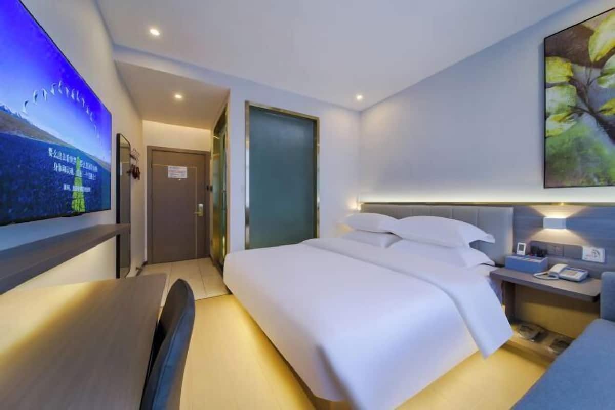 A hotel room with a bed, bedside table, and a TV mounted on the wall.