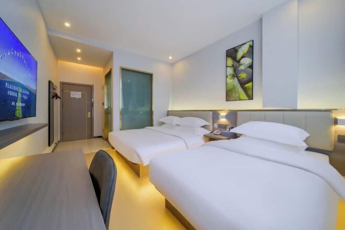 A hotel room with two beds, a desk, a TV, and a painting on the wall.