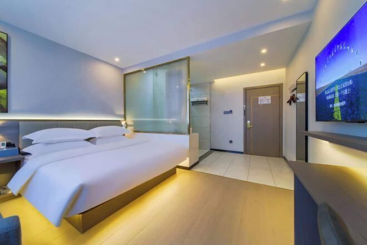 A modern hotel room with a large bed, a flat-screen TV, and a glass partition wall.