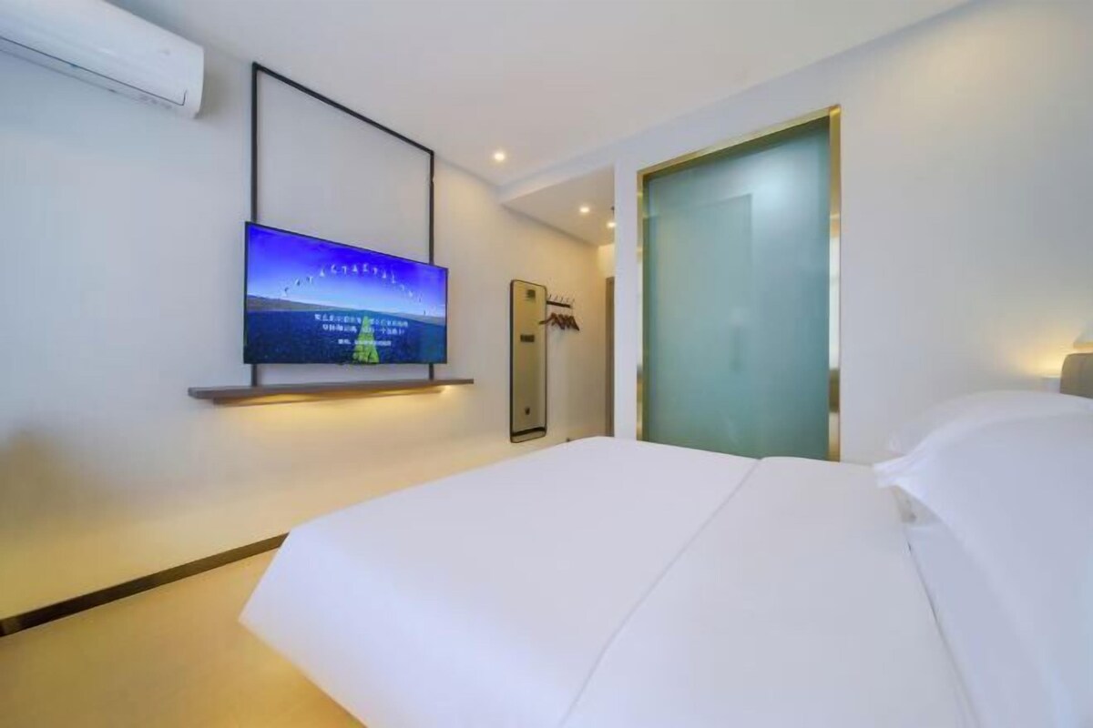 A hotel room with a bed, a mounted TV, a coat rack, and a door with frosted glass.