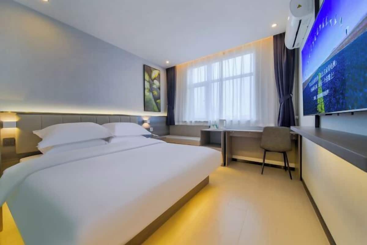 A modern hotel room with a large bed, a desk, and a TV.
