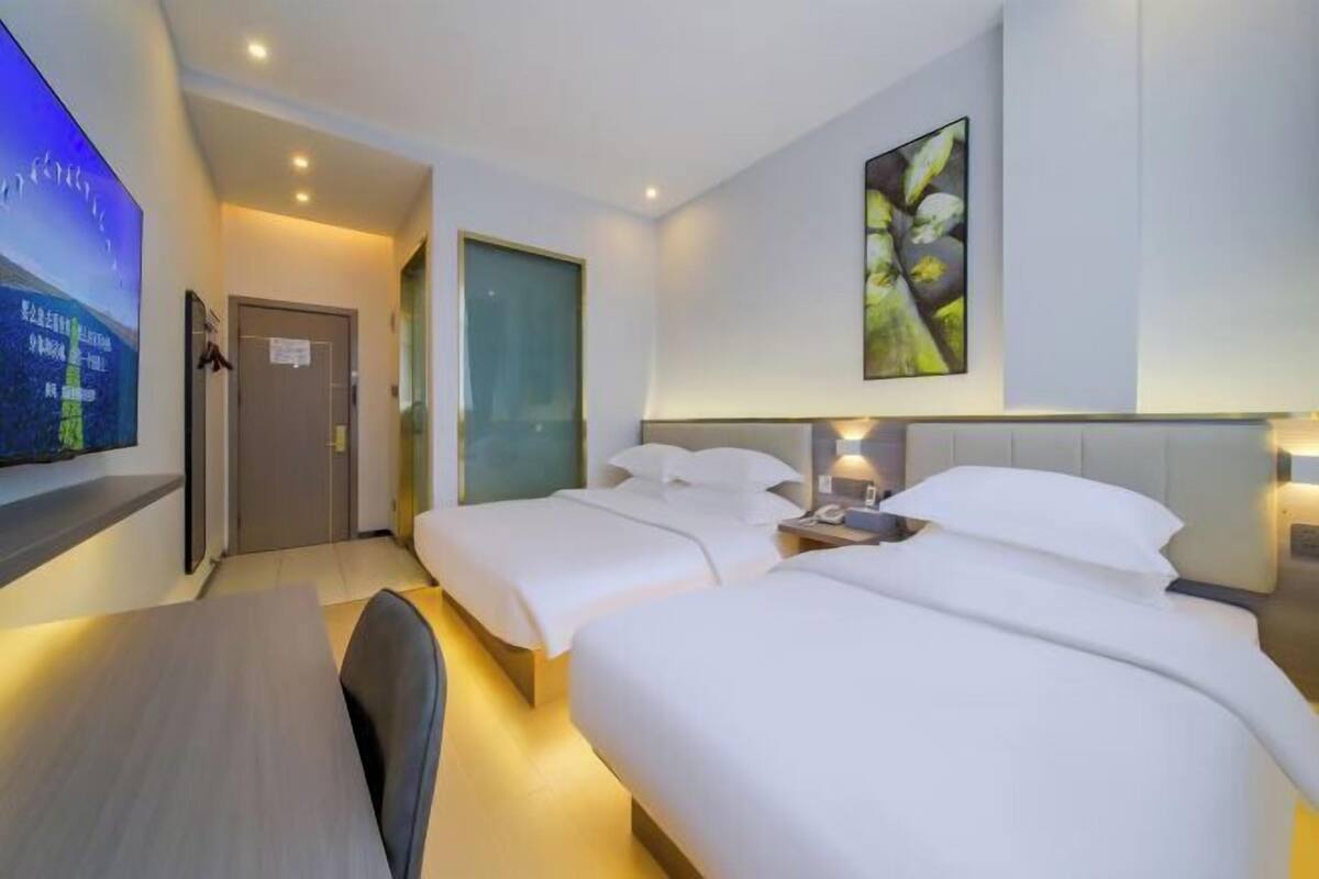 A hotel room with two beds, a desk, a TV, and a painting on the wall.