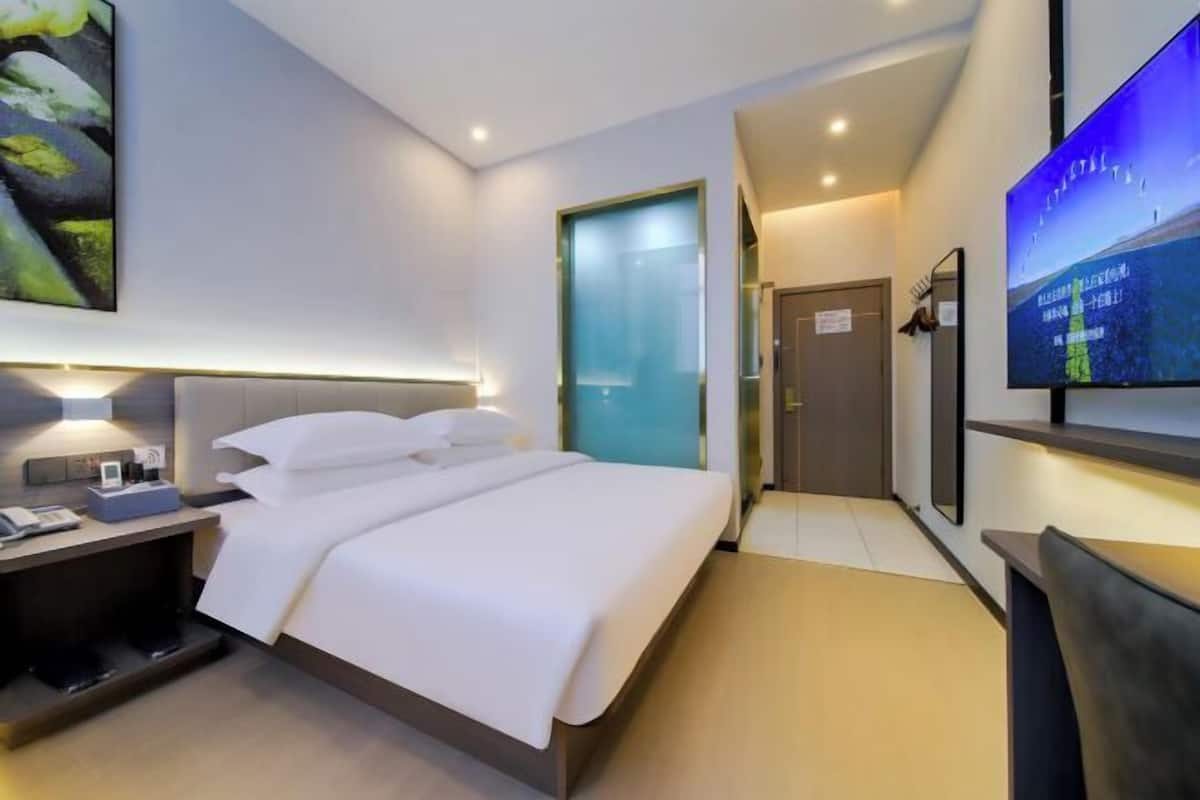 A modern hotel room with a large bed, bedside table with a lamp, a flat-screen TV mounted on the wall, and a painting above the bed.