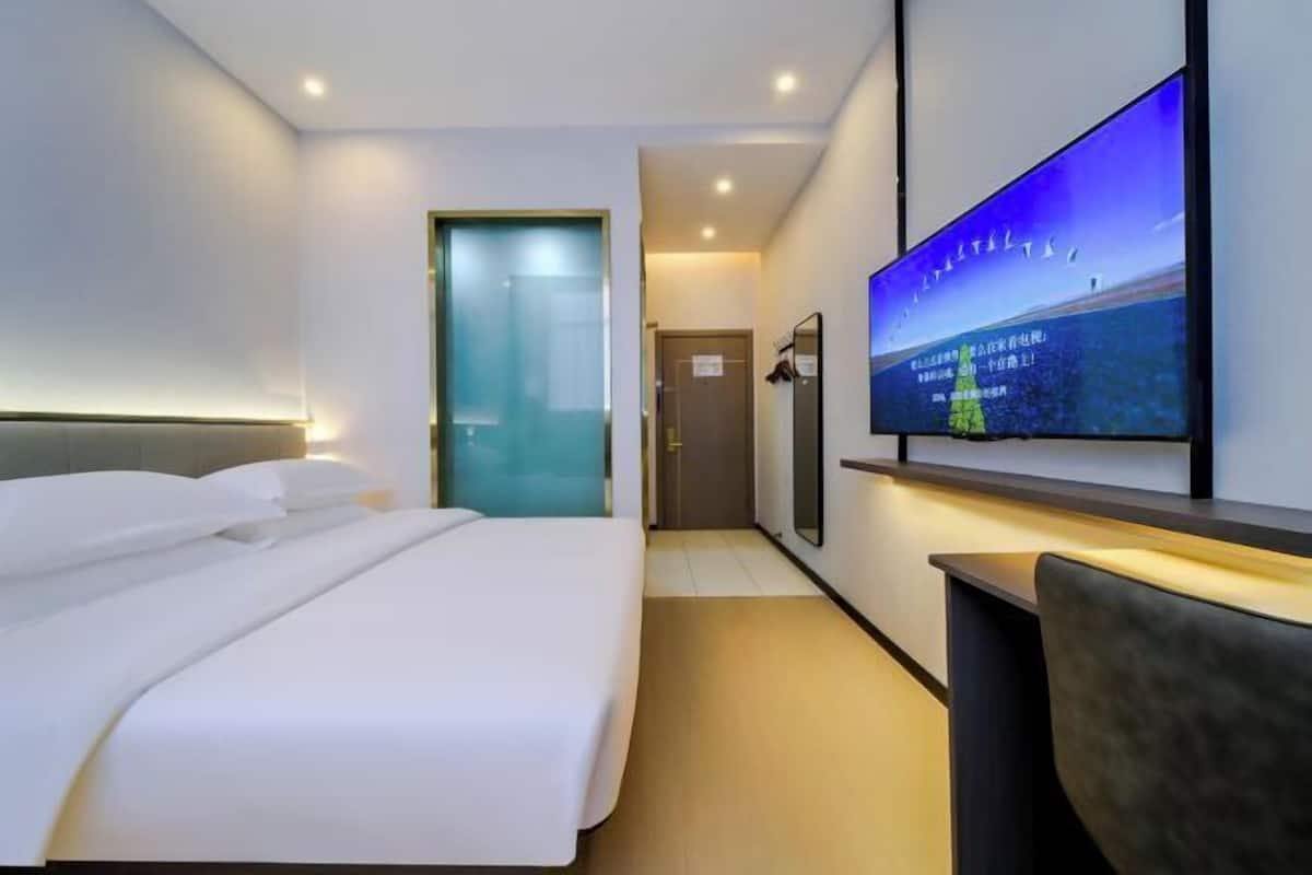 A hotel room with a bed, a TV on the wall, and a door leading to another room.