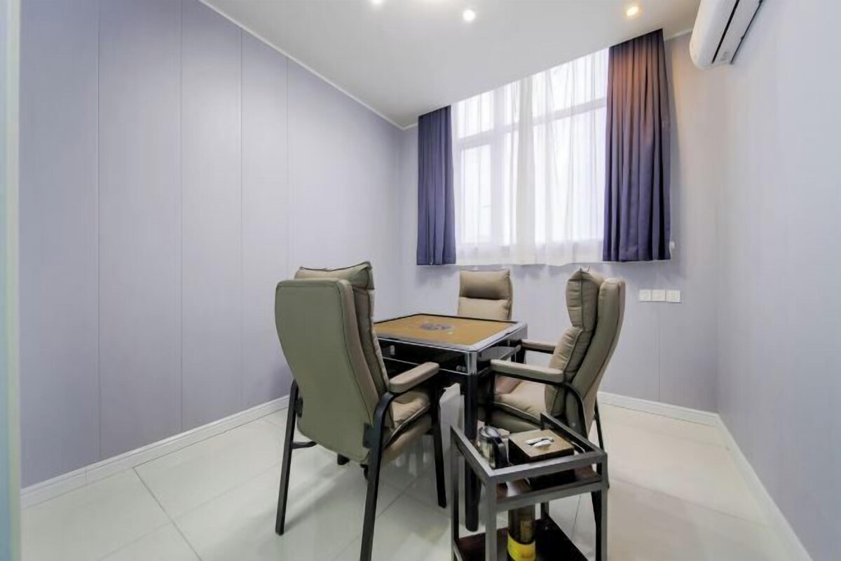 A room with a round table and four chairs, a window with curtains, and an air conditioning unit on the wall.