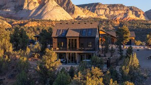 A modern two-story house with large windows and a balcony, surrounded by trees and mountains. - Sunset Pointe| Modern Comfort| Epic Views| Zion (Orderville)
