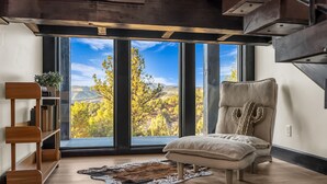 A modern room with a large window, a plush chair, wooden shelves, and a leather rug. - Sunset Pointe| Modern Comfort| Epic Views| Zion (Orderville)