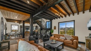 A spacious living area with leather sofas, a coffee table, and a staircase leading to a balcony. - Sunset Pointe| Modern Comfort| Epic Views| Zion (Orderville)