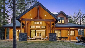 A modern log cabin with a large porch, stone pillars, and a dining area.