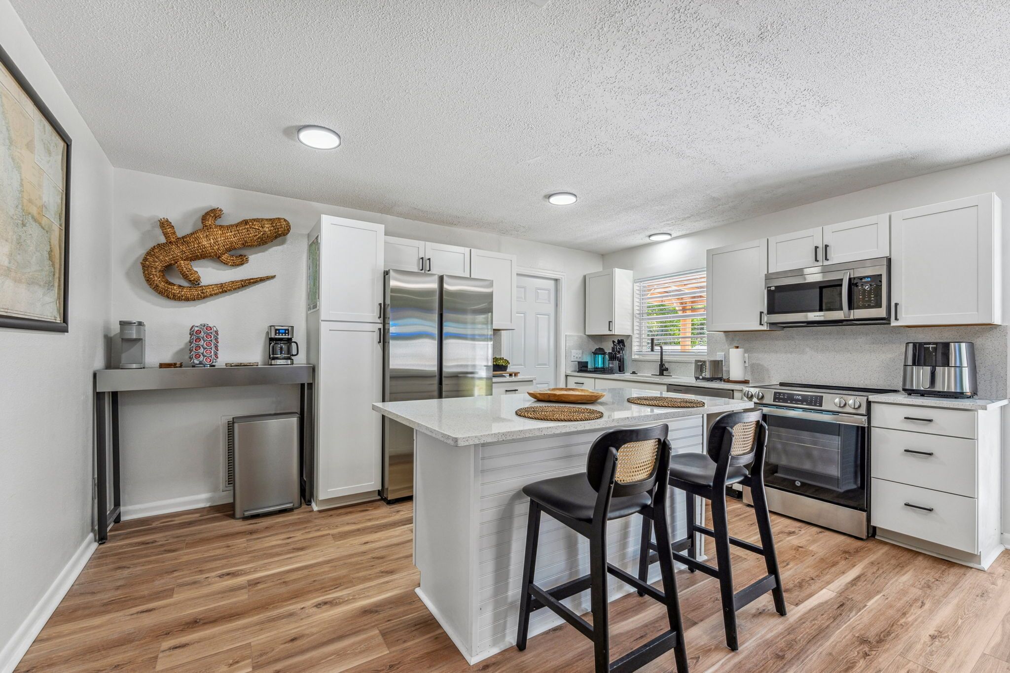 A modern kitchen with white cabinetry, stainless steel appliances, and a central island with bar stools.