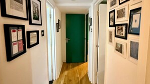 Un couloir aux murs ornés de tableaux encadrés, une porte verte au fond et un plancher en bois.