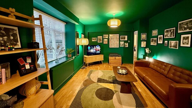Un salon chaleureux avec un mur vert, des meubles en bois, un téléviseur et divers tableaux encadrés.