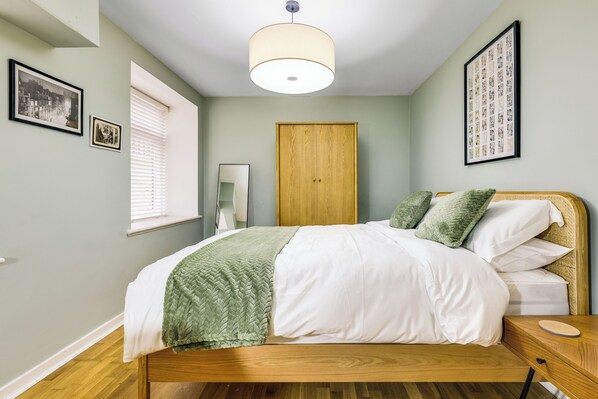 A neatly made bed with a green throw blanket, a wooden headboard, and a bedside table with a round mirror.