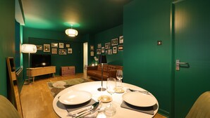 Un coin repas avec une table ronde dressée pour deux personnes, un téléviseur et un canapé, le tout dans une pièce aux murs de couleur turquoise.