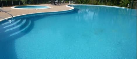 A clear blue swimming pool with a curved edge, surrounded by a paved deck and a few lounge chairs.