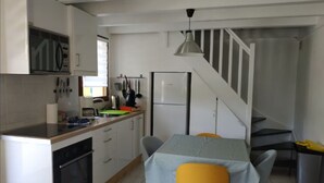 A compact kitchen with white cabinets, a built-in oven, and a dining area with a table and chairs. - Quiet 3*** listed vacation home with swimming pool (Saint-Julien-en-Born)