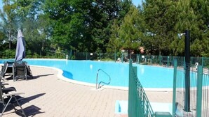 A swimming pool with a green fence, surrounded by trees and a covered seating area with chairs. - Quiet 3*** listed vacation home with swimming pool (Saint-Julien-en-Born)
