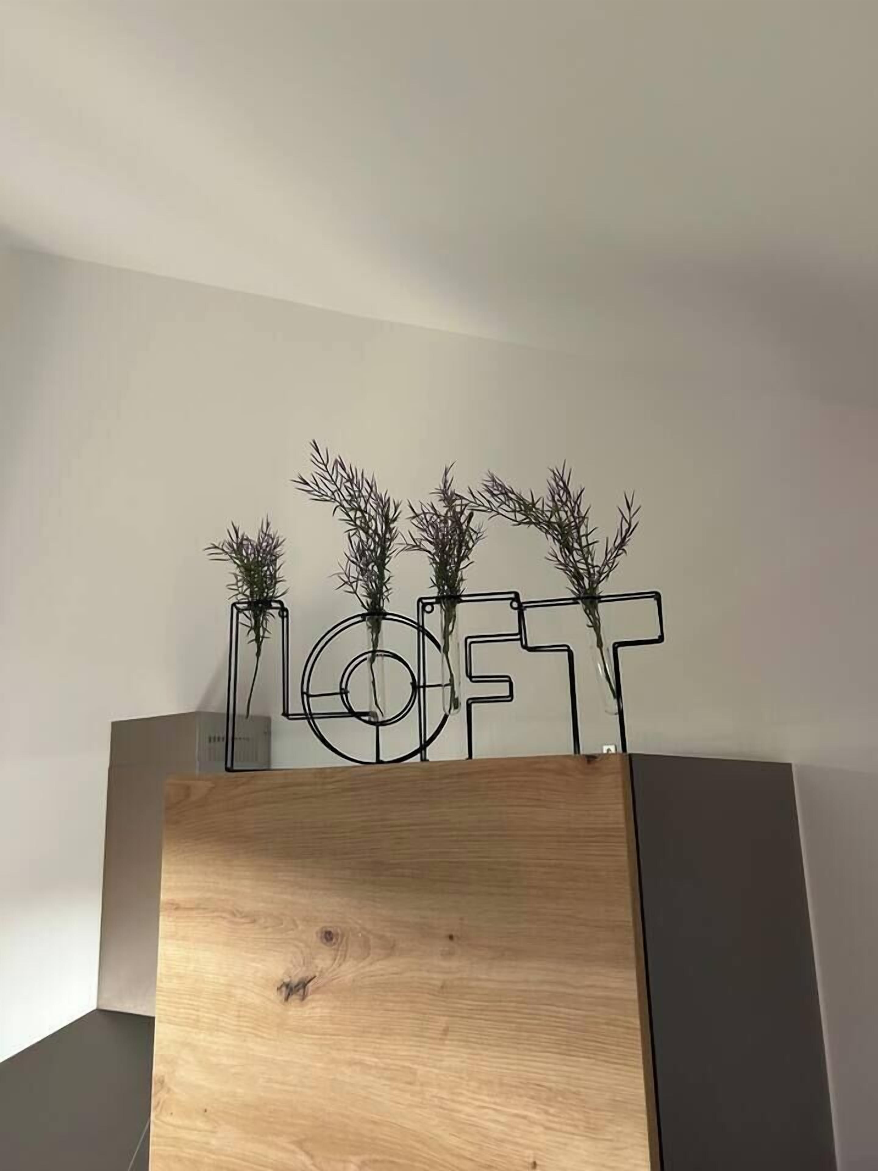 Een modern interieur met een houten paneel en een metalen bord waarop 'LOFT' staat, met kleine planten.