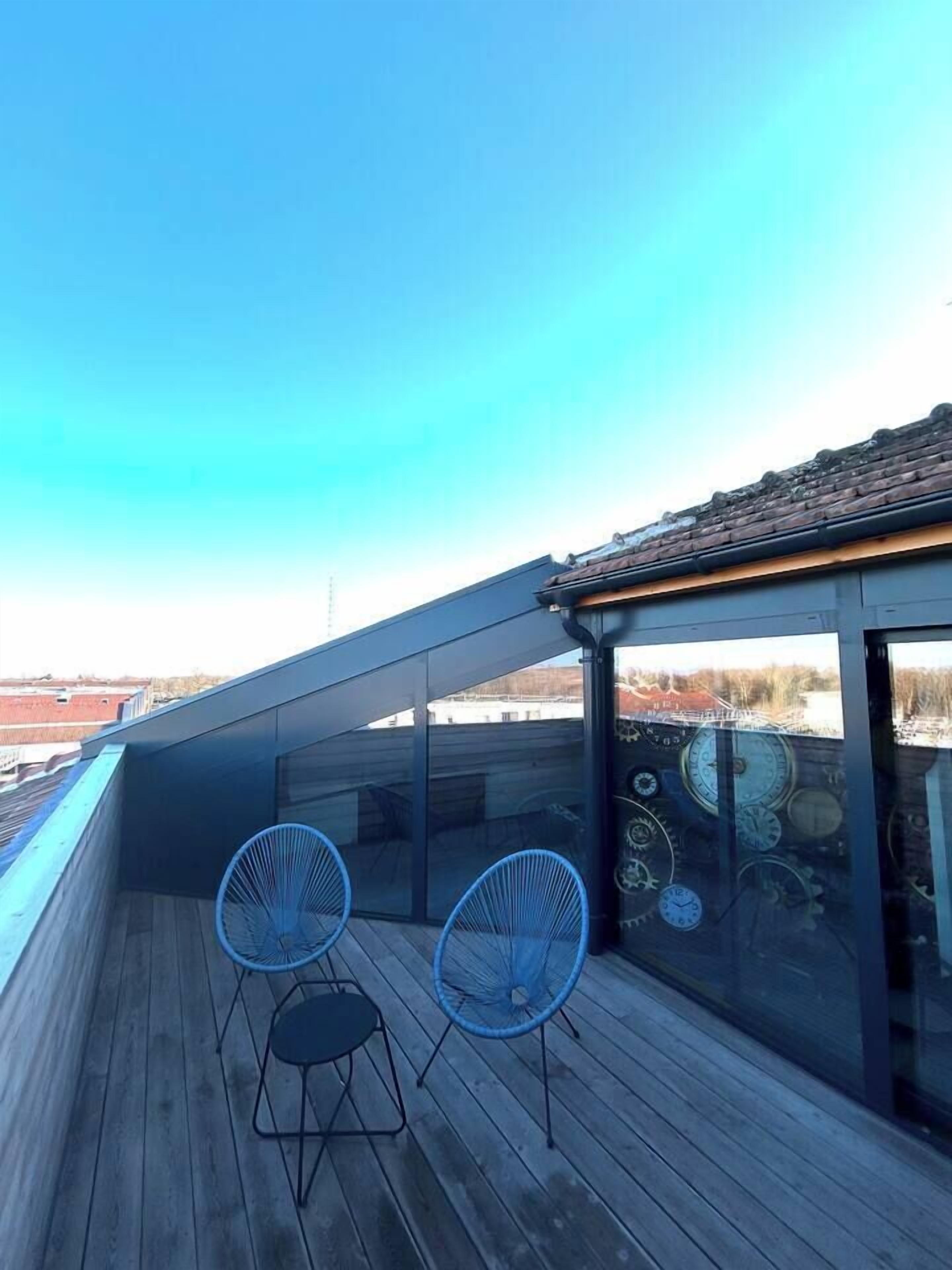 Eine Dachterrasse mit zwei blauen Stühlen und einem Tisch, einem Holzboden und Blick auf die Stadtlandschaft.