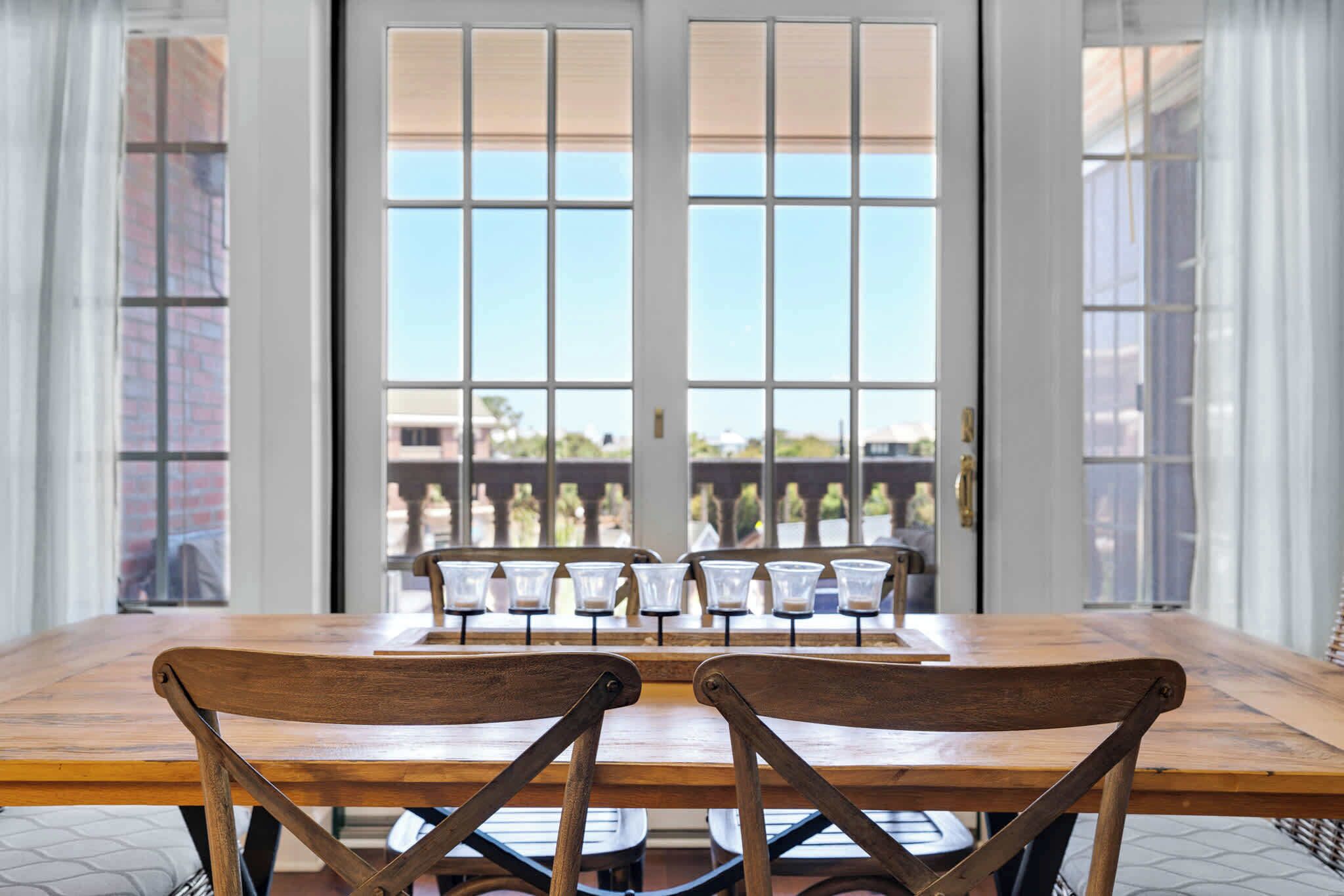 Un coin repas avec une table et des chaises en bois, de grandes fenêtres équipées de stores et une vue sur les bâtiments environnants.
