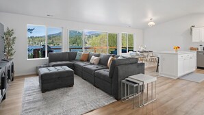A modern living room with a sectional sofa, a small table, and a view of a lake and mountains.