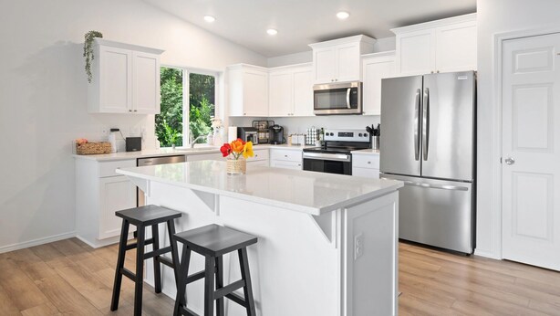 A modern kitchen with white cabinetry, stainless steel appliances, and a central island with stools.
