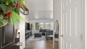 A modern living room with a grey sectional sofa, a coffee table, and a TV. There is a wooden floor and a white door on the right.