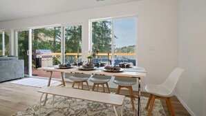 A modern dining area with a large table set for four, large windows, and a view of the outdoors.