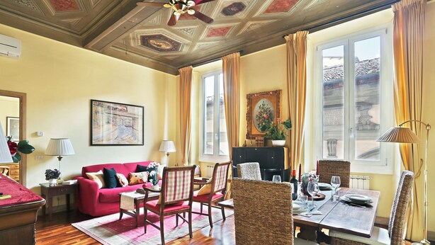 A living room with a red sofa, wicker chairs, a dining table set for two, and a fireplace.