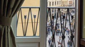 A view from a window with a curtain, overlooking a busy street with pedestrians and buildings.