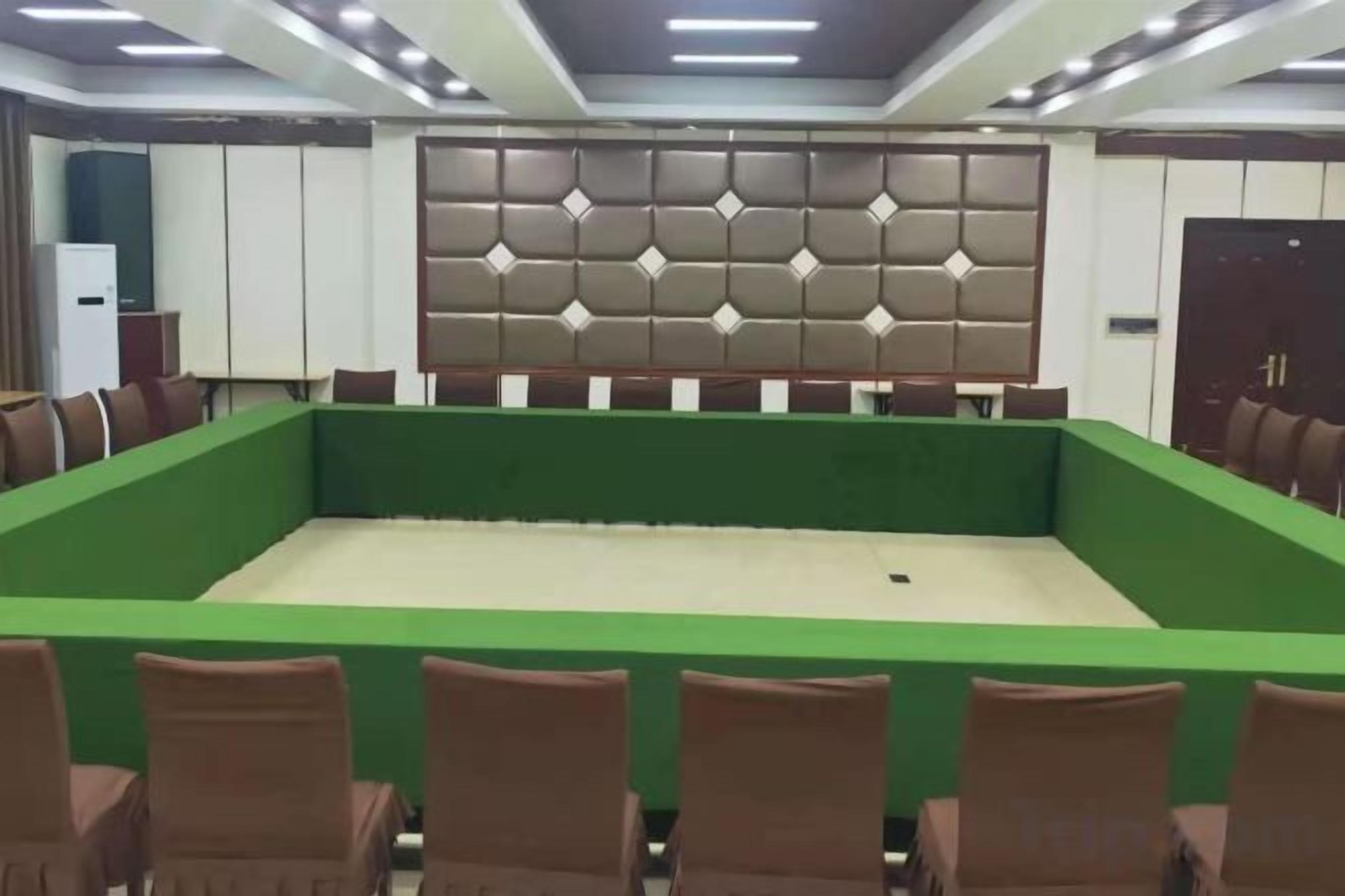 Un salón de conferencias con una mesa verde, sillas marrones y una pared acolchada.