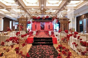 Un salón amplio con un escenario central, decoraciones ornamentales y una alfombra de flores rojas.