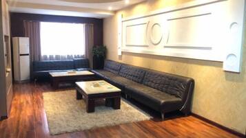 A living room with a sofa, a coffee table, a refrigerator, and a large window.