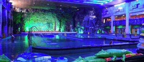 Una amplia piscina interior con varias pistas, rodeada de decoración temática tropical y una cascada.