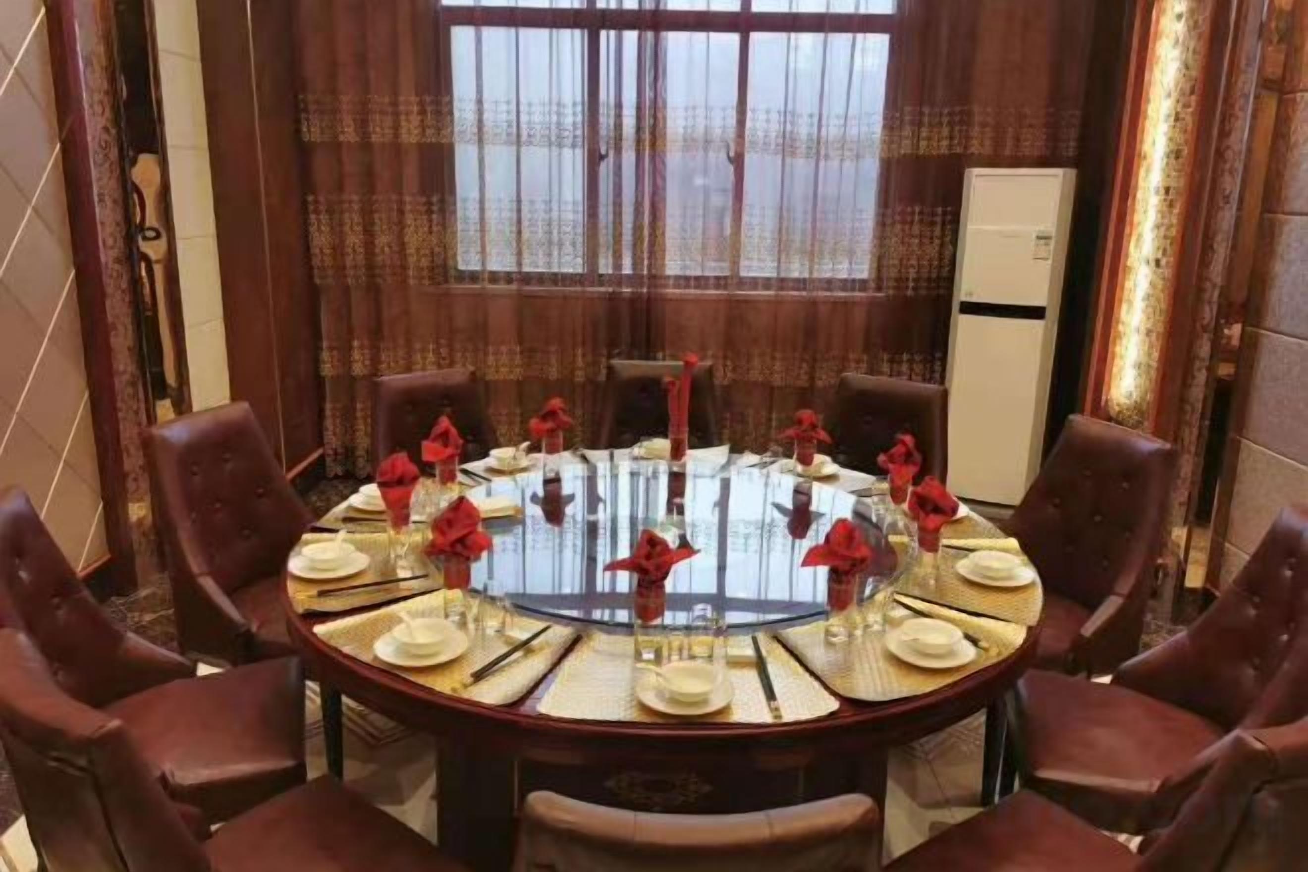 Una mesa de comedor redonda con sillas, cubierta con platos blancos, servilletas rojas y copas de cristal.