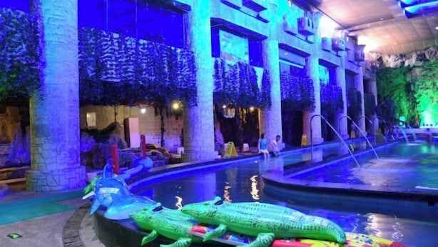 A swimming pool area with a large inflatable crocodile and a dolphin, surrounded by columns and greenery. - Xinxiang Jinghua Tropical Mineral Spring Health Garden (Xinxiang County)