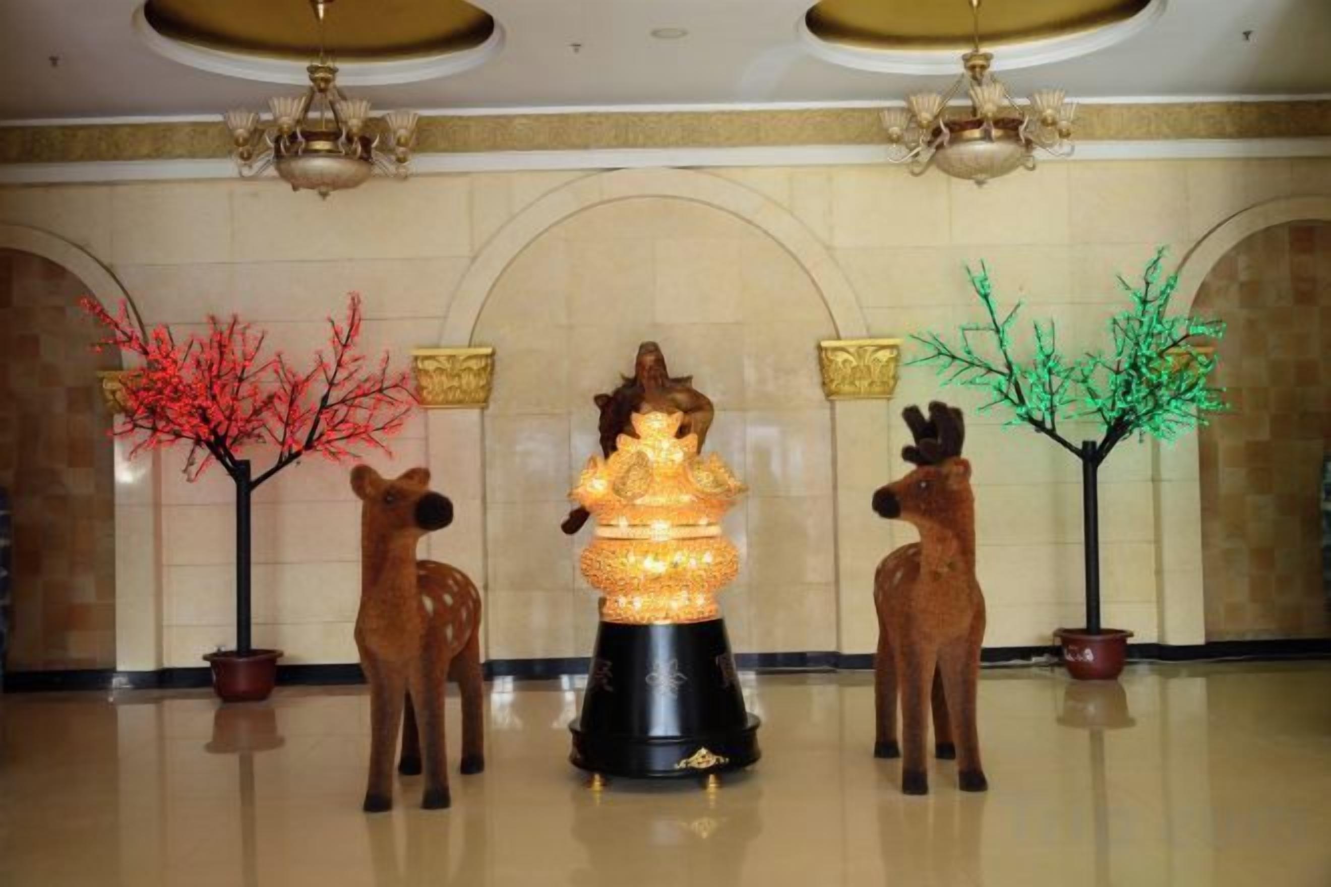 A lobby with a central statue, two deer statues, and two illuminated trees.
