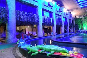 Un área de piscina con una gran escultura de cocodrilo, plantas de interior y un diseño arquitectónico moderno.