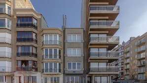 A row of modern multi-story residential buildings with balconies, a central building with large windows, and a clear sky. - Renovated Ground-floor Apartment in Koksijde (Koksijde)