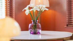 Un coin repas avec une table ronde, un vase de fleurs blanches et des luminaires suspendus.