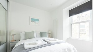 A bedroom with a bed, two bedside tables, a window, and a painting on the wall.