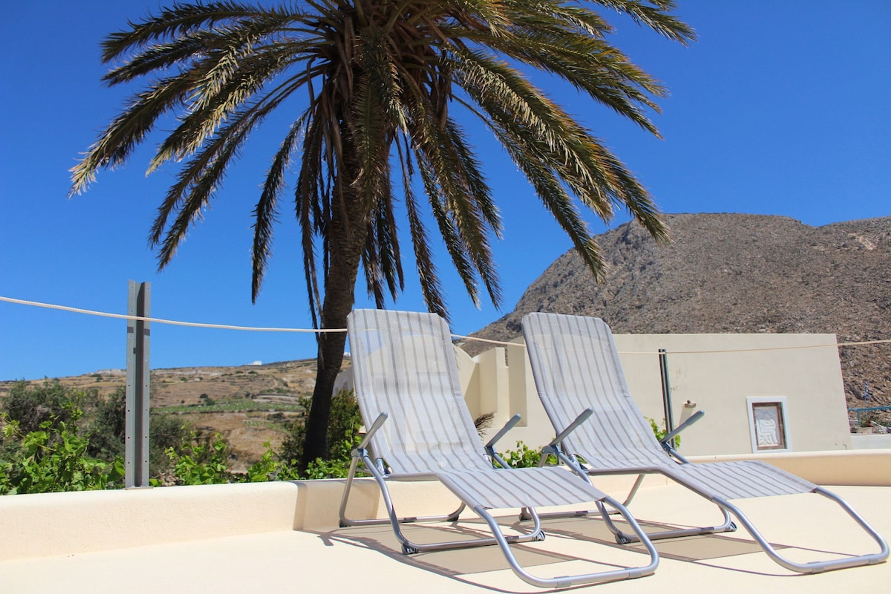Dos sillones de descanso con estructura metálica y tela a rayas, ubicados en un balcón con vista a una palmera y una montaña al fondo.