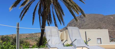Dos sillones de descanso con estructura metálica y tela a rayas, ubicados en un balcón con vista a una palmera y una montaña al fondo.