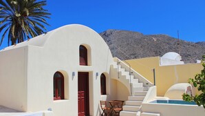 Um edifício branco com uma porta vermelha e uma escadaria que dá acesso a uma área de piscina.