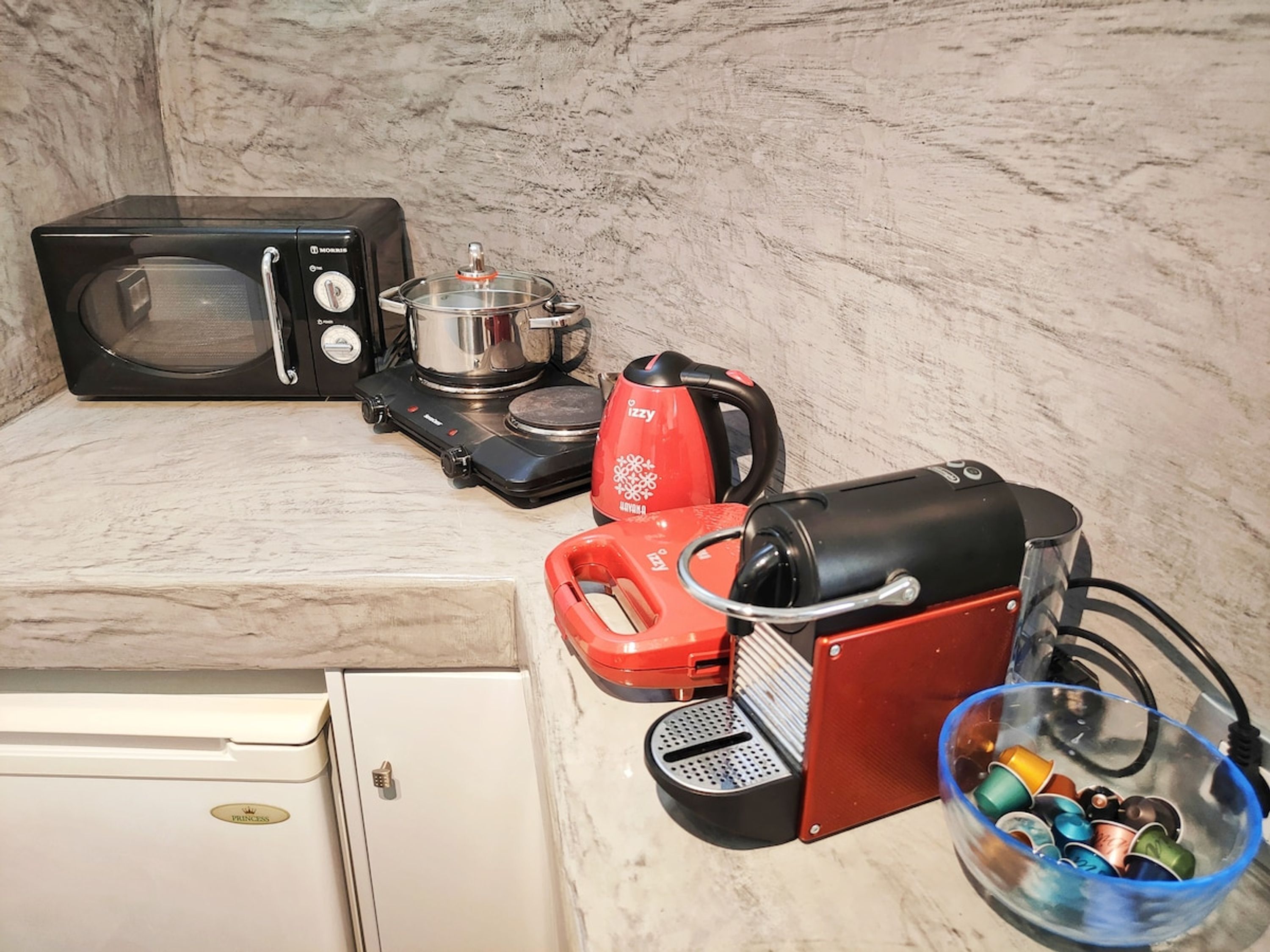 Eine Küchenzeile mit Mikrowelle, Wasserkocher, Toaster und kleinem Kühlschrank.