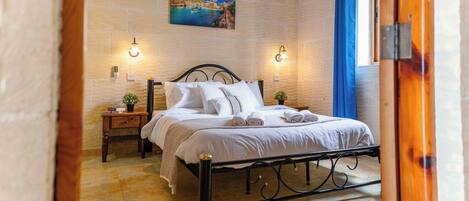 Una cama bien hecha con ropa de cama blanca, dos mesitas de noche con lámparas y un cuadro de una escena costera en la pared.