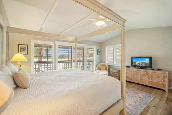 A bedroom with a four-poster bed, a television, a dresser, and a balcony with a view.