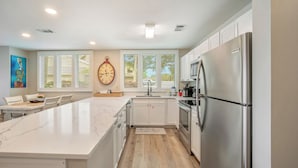 A modern kitchen with a large island, stainless steel appliances, and a clock on the wall. - Seascape Boardwalk Villa 199*5 minute walk to beach! (Miramar Beach)